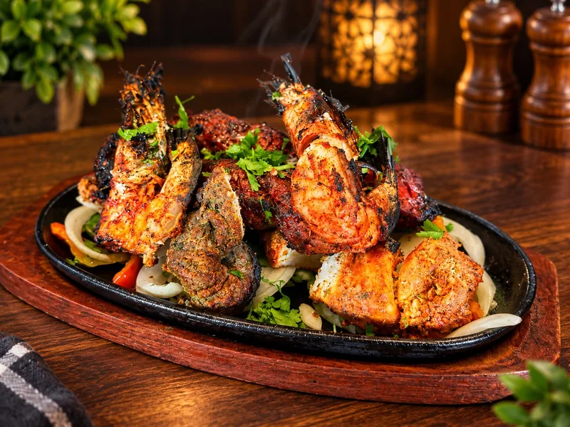 Tandoori Mixed Grill : gambas, agneau tikka, seekh kebab et poulet tandoori servis fumants sur leur plat en fonte